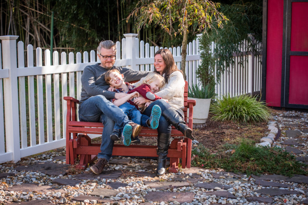 Two kids sitting in between their parents and laughing in their backyard 