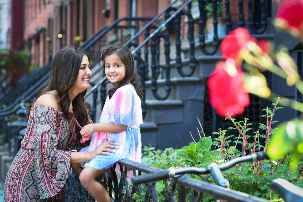 A small girl sitting on a railing being held up by her mother 