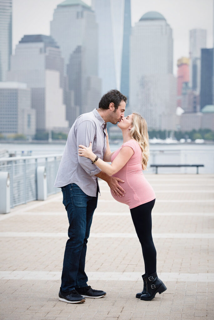 An expecting couple kissing with the NYC skyline in the distance 