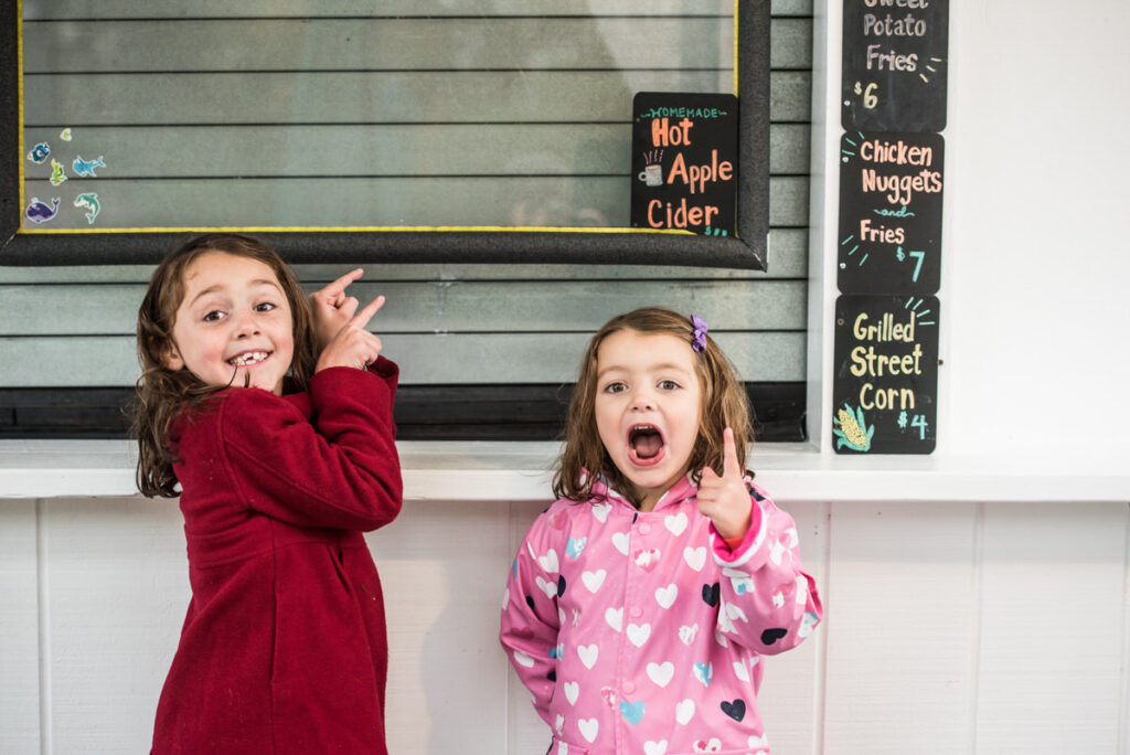 Two girls smiling and pointing to a sign that says "hot apple cider"