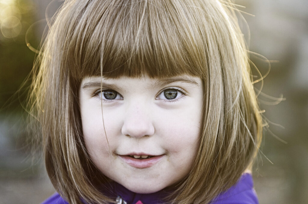 Close up of a young girl, smiling coyly, with golden light on hair