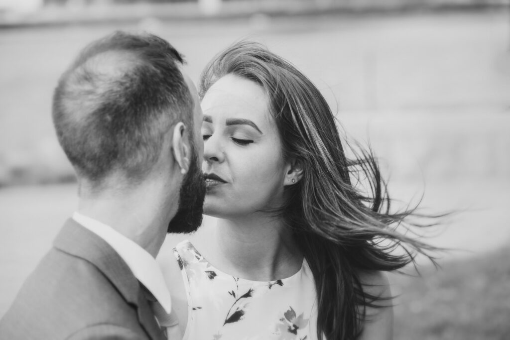 A black-and-white image of a couple about to kiss, with the woman's hair gently blowing in the wind.