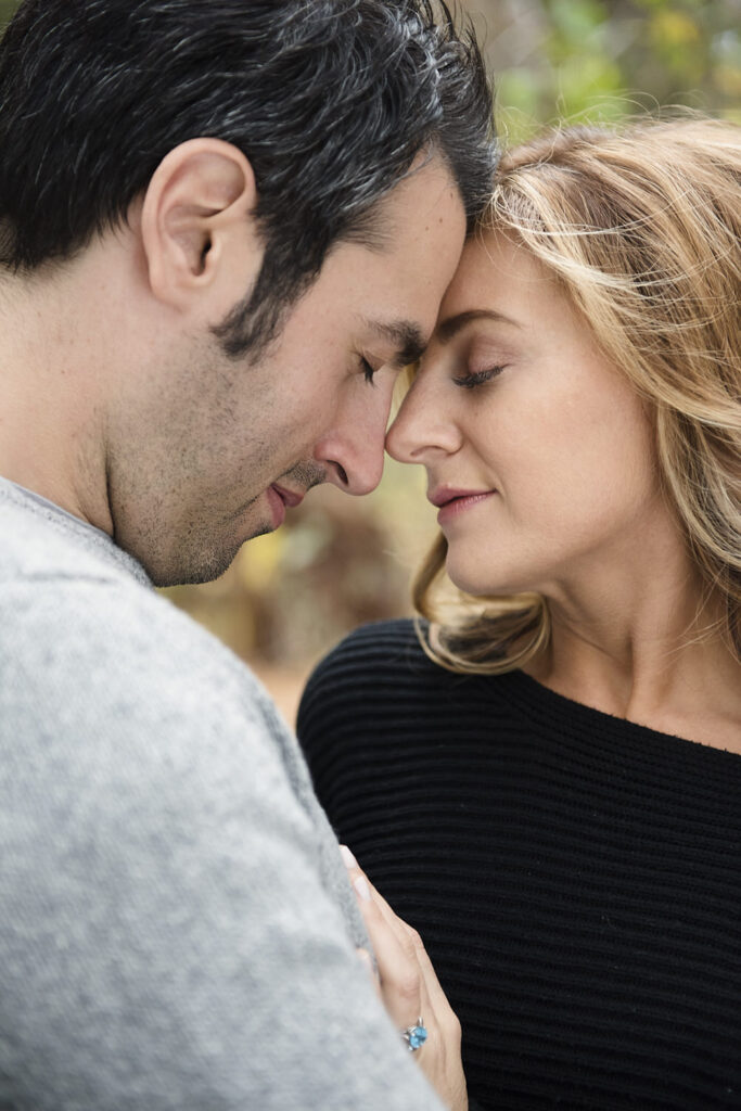 A close-up of a couple touching foreheads with eyes closed, sharing an intimate moment outdoors.