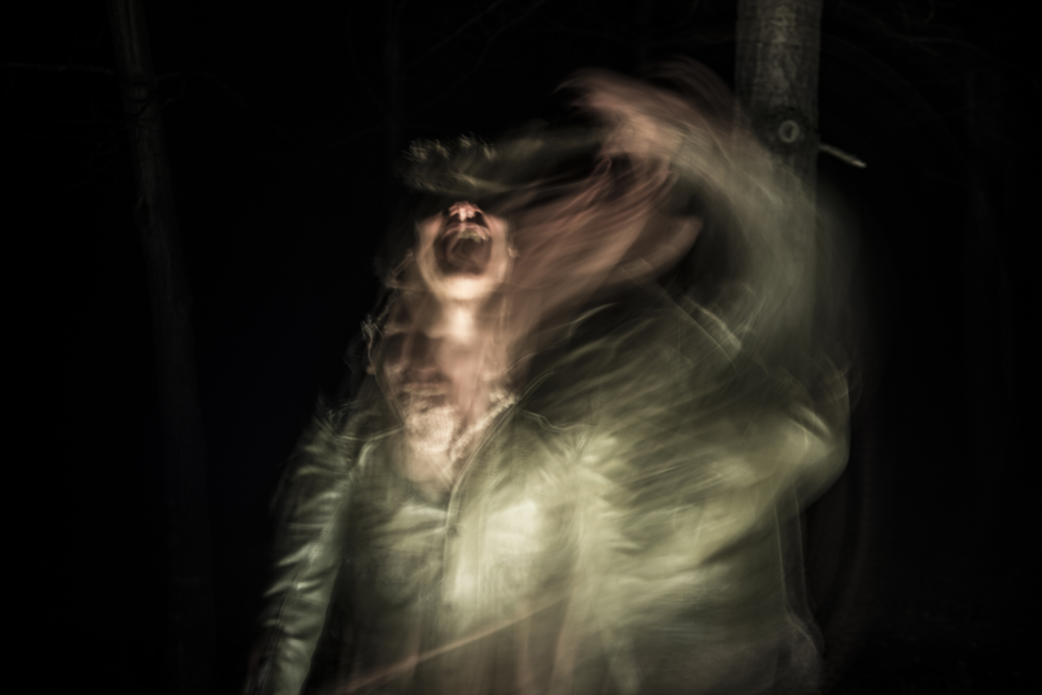 A blurred figure in motion appears to scream, creating a ghostly effect in the dark with overlapping faces and hands.