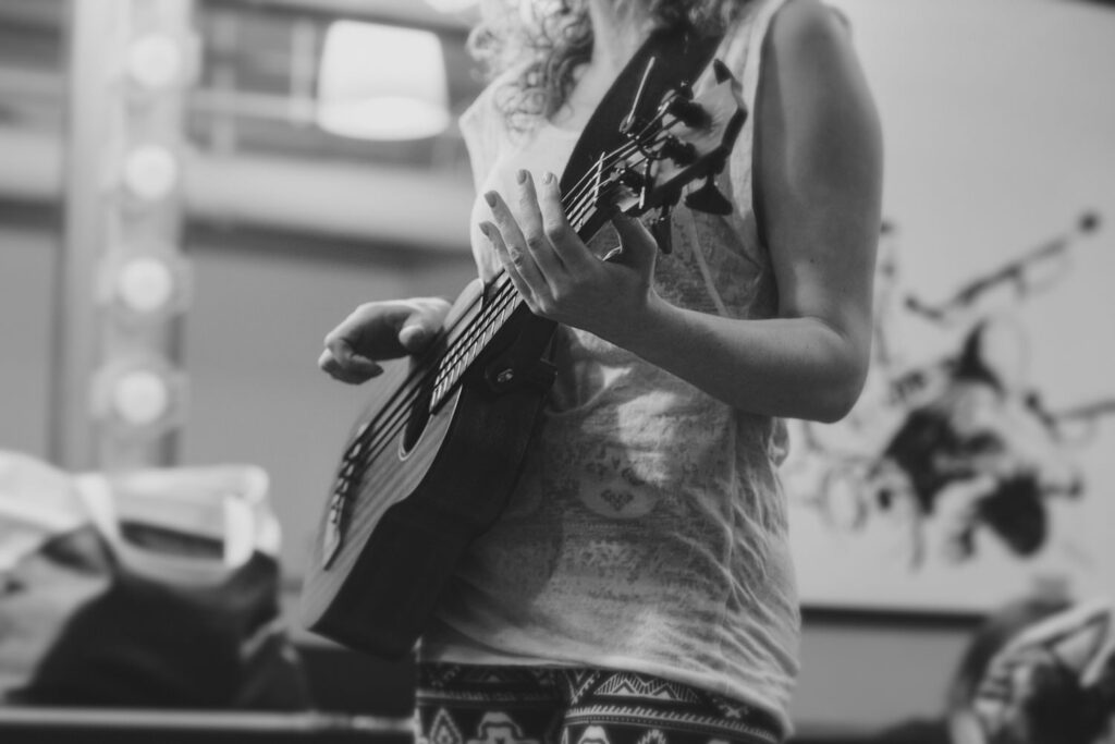 A person strums a guitar, focusing on the hands and instrument, with a soft, blurred background.