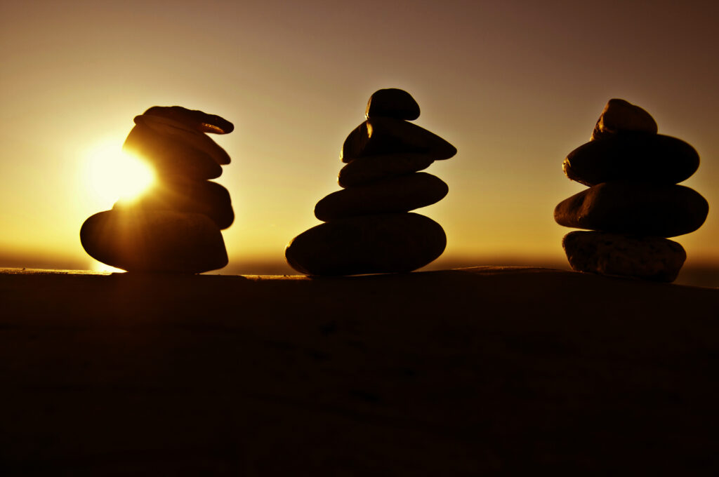 Silhouetted stone stacks against a sunset, creating a serene and balanced scene as the sun sets behind them.