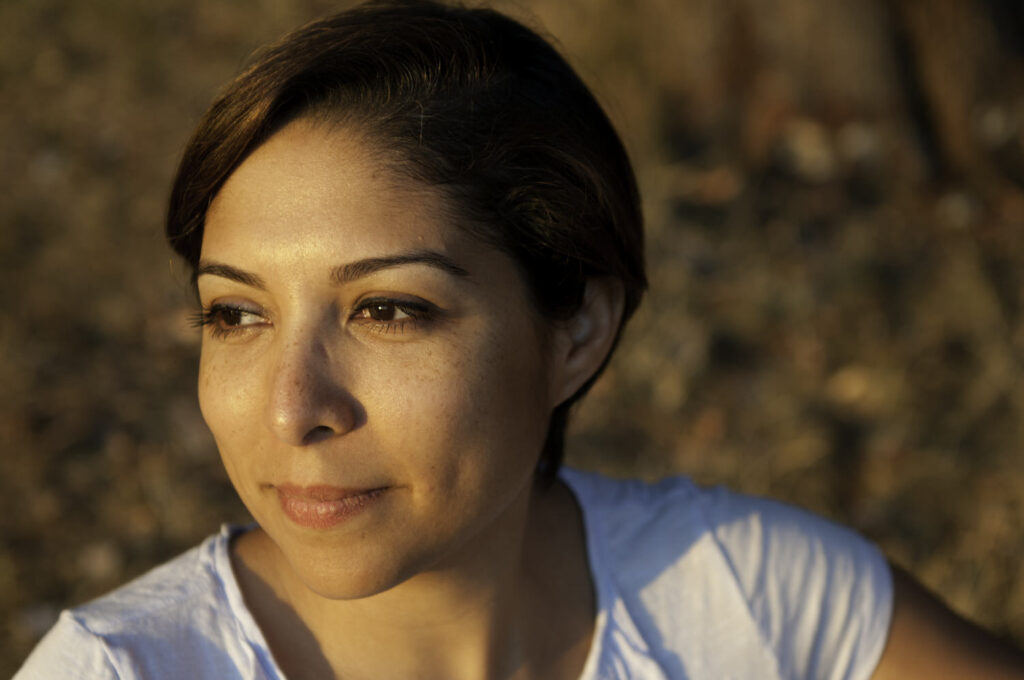 A close-up portrait of a woman with short hair looking off into the distance, bathed in the warm light of golden hour.