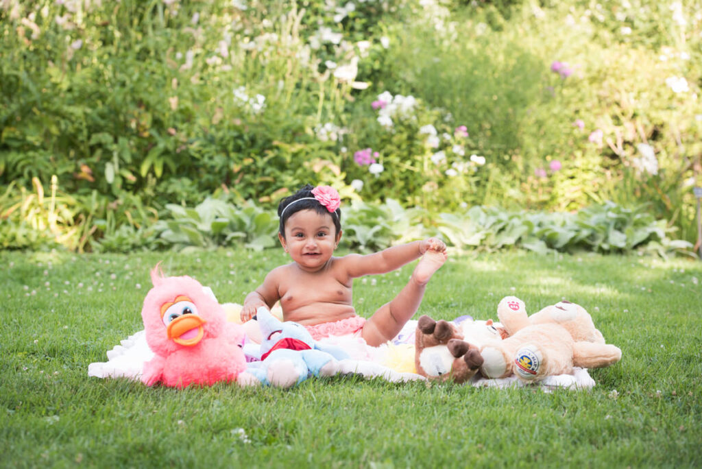 A baby sitting on a picnic blanket holding one leg up
