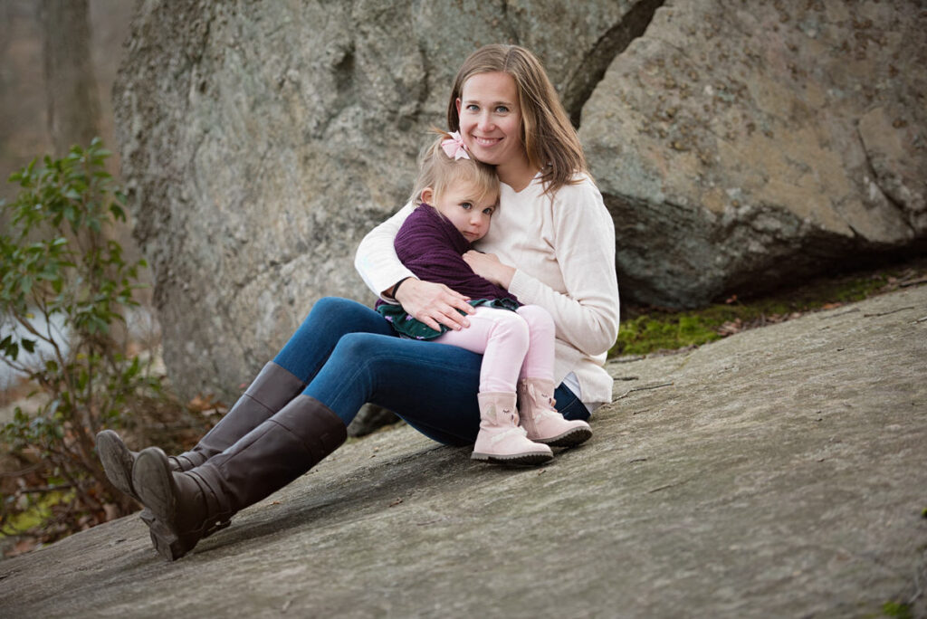 A child sitting on her mother's lap as they are on a rock 
