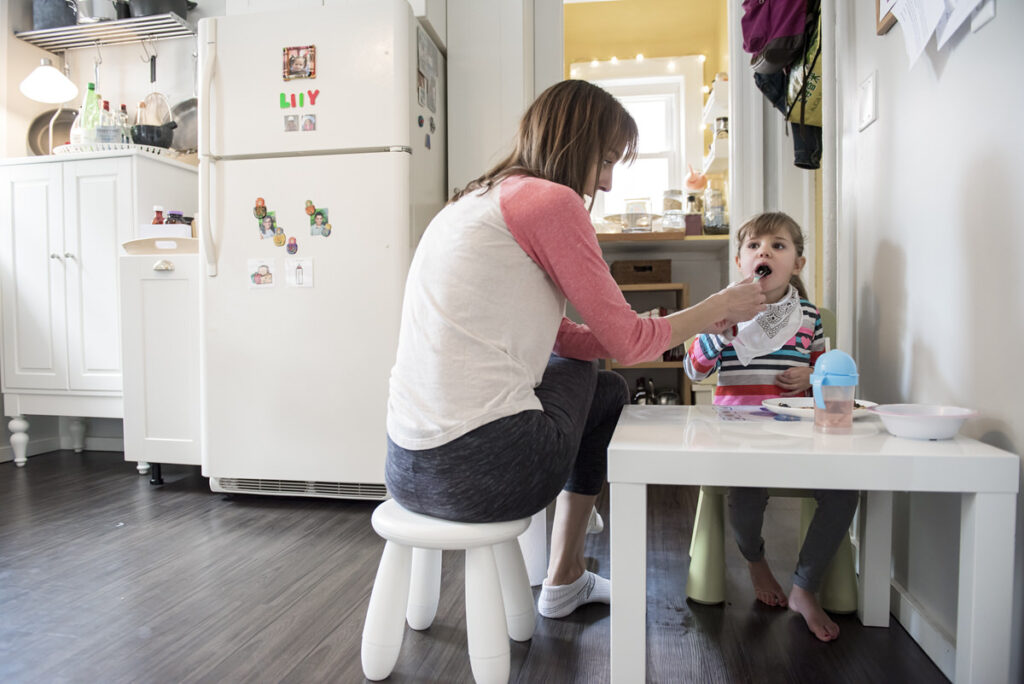 A mom feeding a small girl while sitting at a child's table 