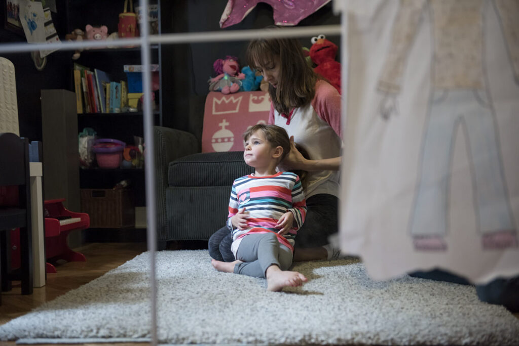 A parent sitting on the floor as they do their child's hair 