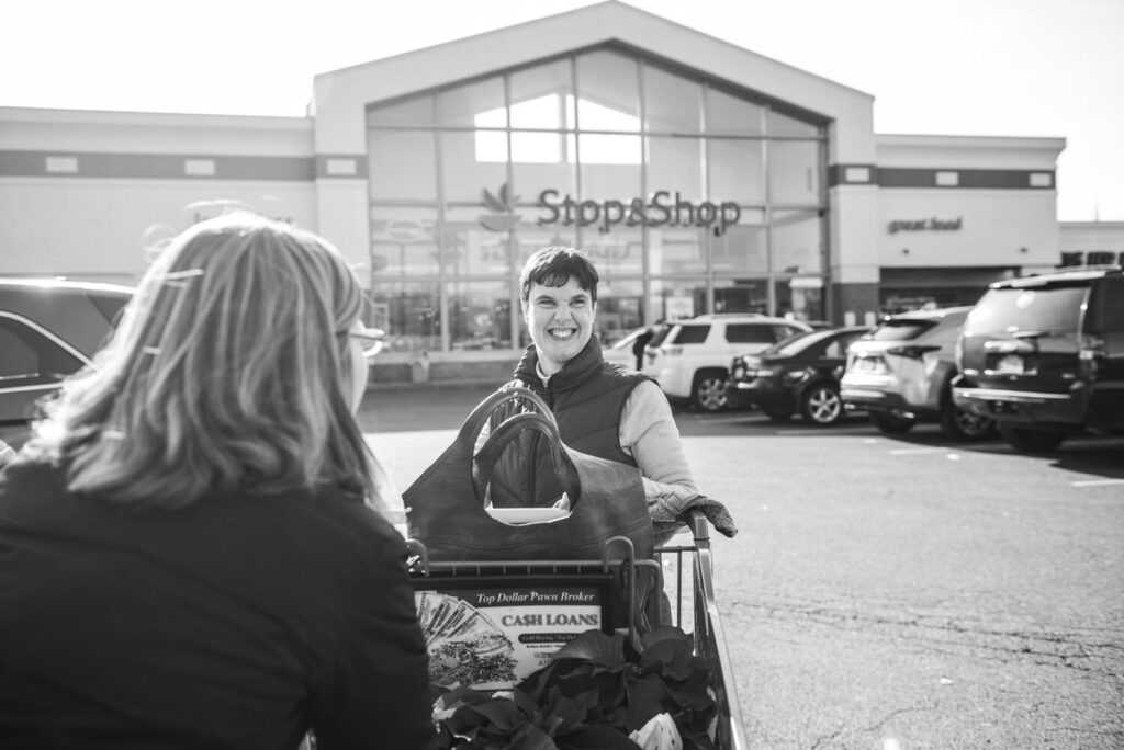 A child smiling as they stand in front of a grocery store with their parent
