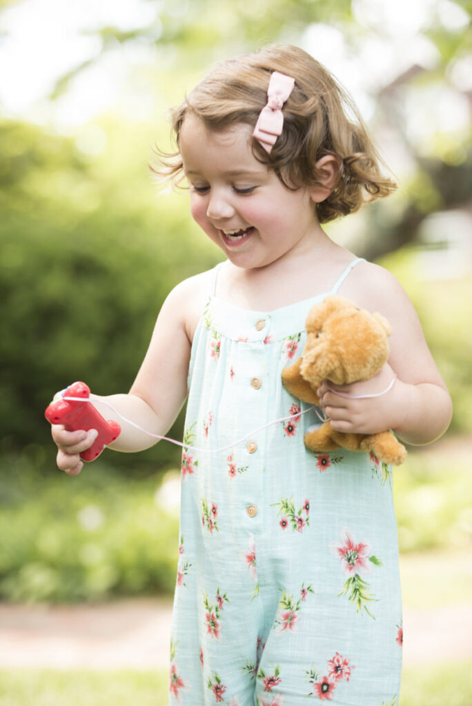 A small girl smiling and holding a stuffed animal 
