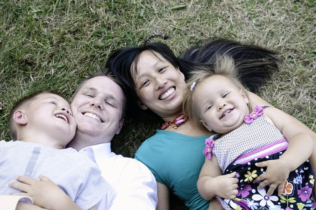 Parents laying on the grass with their kids laying on top of them 
