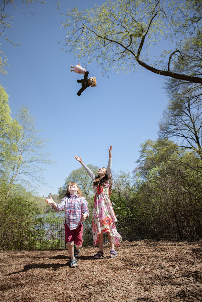 Two kids throwing their stuffed animals into the air 