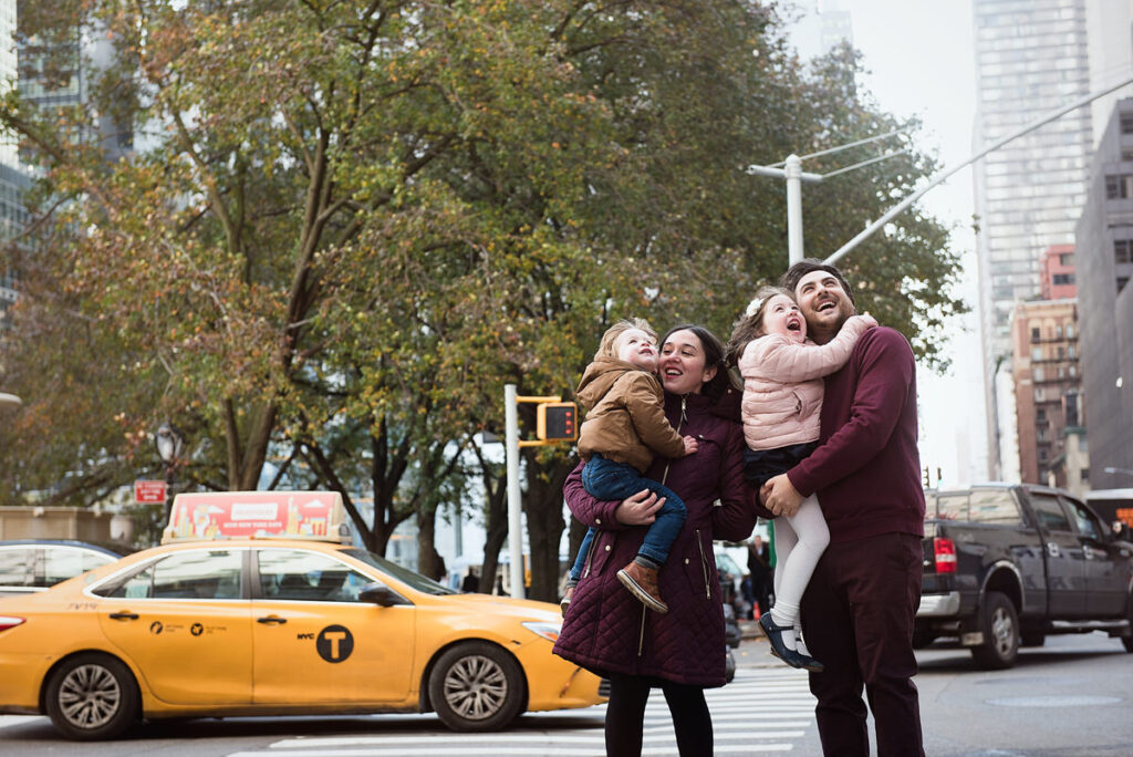 Two parents each holding small children and smiling in a city 