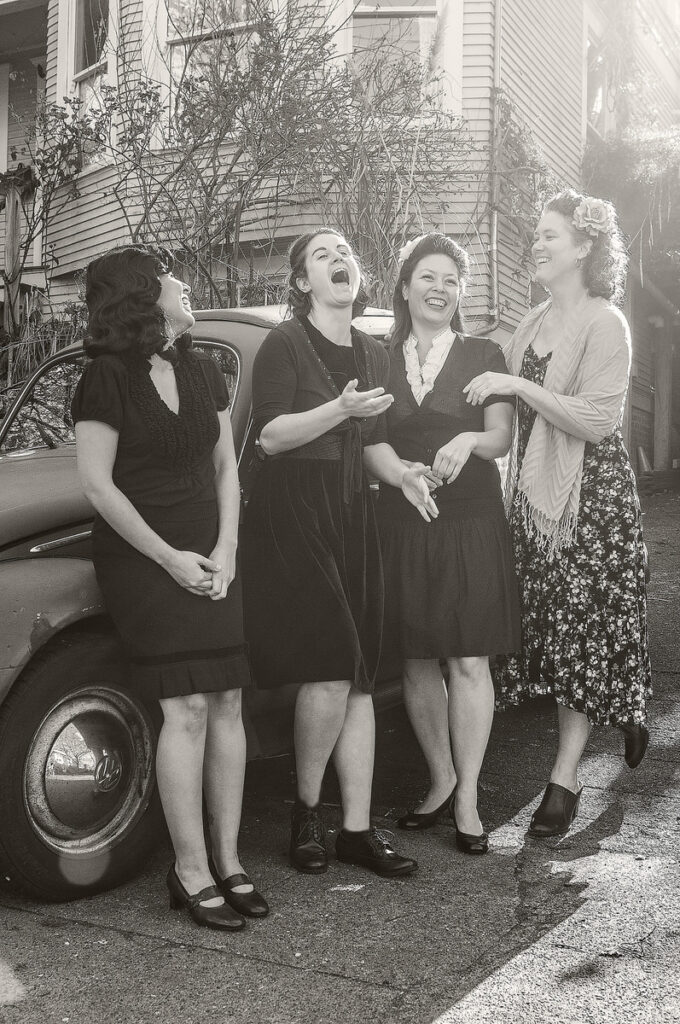 A group of women laughing next to a vintage car 
