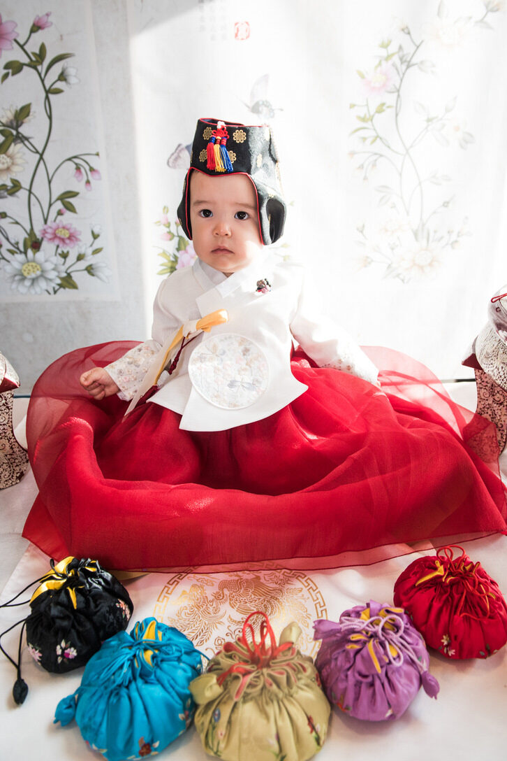 A baby in a traditional Asian outfit with colored sacks in front of her 